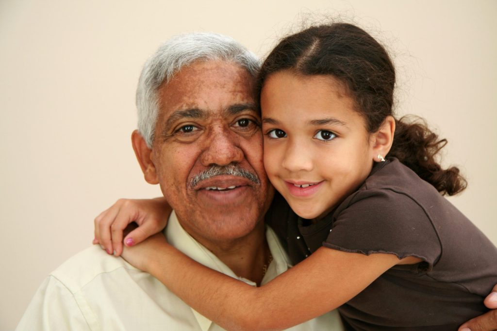 Young girl hugging senior man with arms around his neck