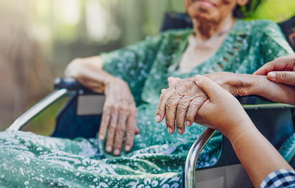 Woman in wheelchair with person kneeling beside her holding her hand